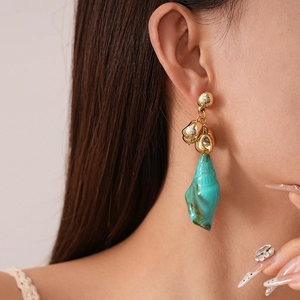 Close-up of model wearing gold irregular metal beads and teal resin shell earrings