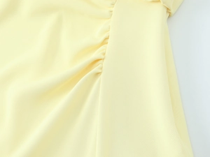 Macro view of light yellow midi dress showing detailed ruched side seams and woven texture