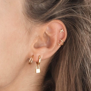 Vue détaillée de la boucle d'oreille cadenas dorée et puce en X sur oreille femme