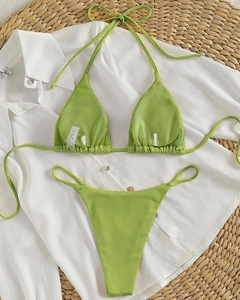 Flat lay detail of grass green ribbed halter bikini set on a white shirt and woven mat