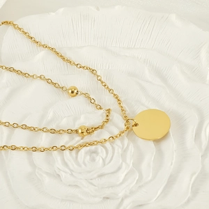 Detail of layered gold double strand necklace with polished round pendant and small beads