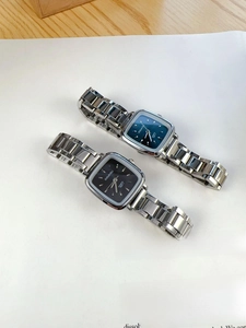 Detailed flat lay of luxury square quartz watches with teal and black dials on a magazine