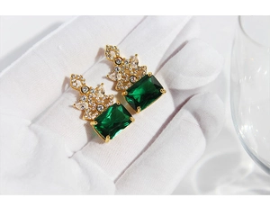 Detail of vintage emerald green gemstone earrings with zircons held in white gloves