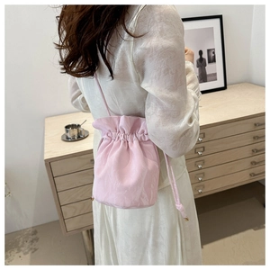 Detail of pink drawstring bucket bag shown on model in a modern minimalist indoor setting
