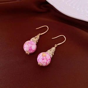 Dettaglio di orecchini vintage in resina rosa marmorizzata con accenti dorati brillanti