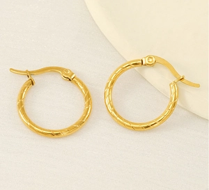 Macro view of gold-plated twisted hoop earrings with hinged closures on white fabric