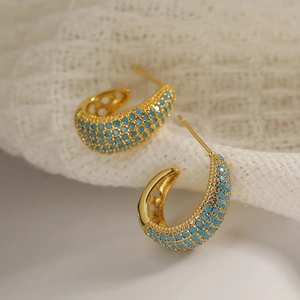 Macro shot of gold-plated C-shaped earrings with turquoise stones on lace background