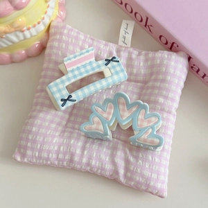 Detail view of floral checkered bow and heart pattern acrylic hair claw clips on a pillow