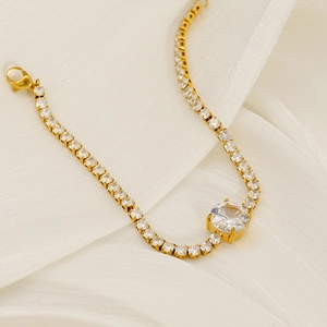 Close-up of golden tennis bracelet with large round zircon center on white silk fabric