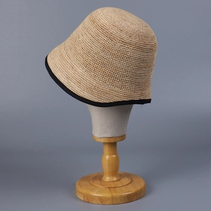 Detail of raffia straw bucket hat with black contrast brim on wooden display stand