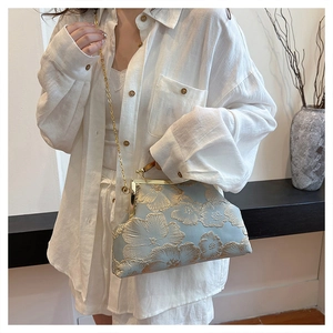Macro shot of light blue satin evening bag with golden 3D flower embroidery and metal chain