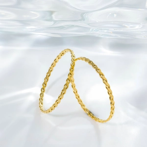 Detail of two gold twist bangles on a luxury water ripple background with elegant lighting