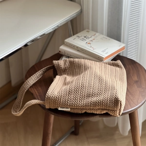 Detailed view of beige knit shoulder bag featuring textured herringbone weaving and brand tag