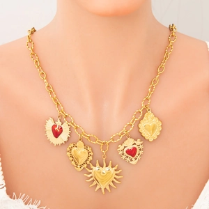 Detail of model wearing a chunky gold necklace with five vintage red heart pendants