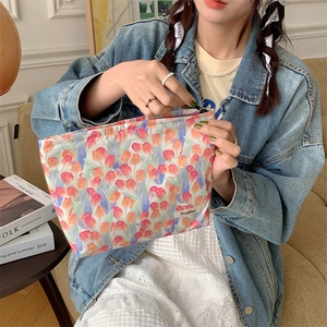 Detail of floral makeup bag with red tulips shown held by a model in casual attire