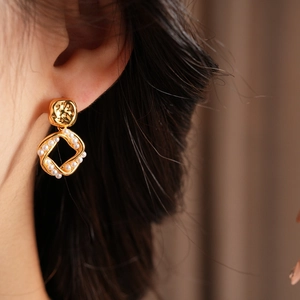 Close-up of elegant gold plated square pearl earring worn by a model in soft lighting