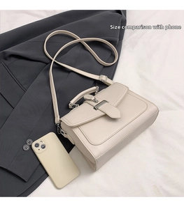 Detail view of cream white crossbody bag with silver buckle and phone for size reference