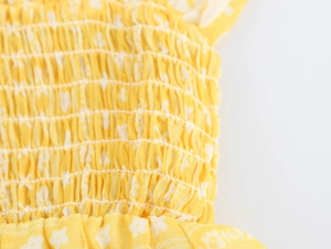 Macro view of yellow floral fabric with elasticated smocked detailing and white print