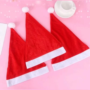 Three red non-woven Christmas hats with white trim and pompoms on a pink background
