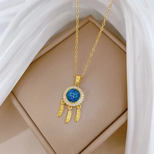 Elegant gold dreamcatcher necklace with blue gemstone and feathers on jewelry box