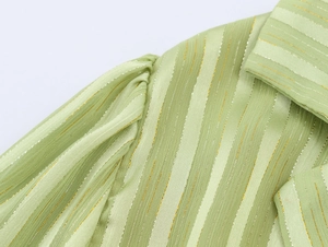 Detailed macro view of light green fabric with gold metallic vertical stripes and soft pleats