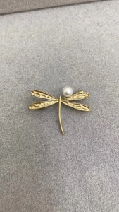Detailed close-up of golden dragonfly brooch with hammered wings and white pearl accent