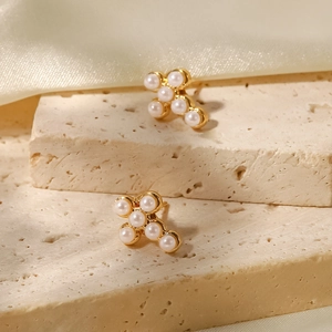 Détails de boucles d'oreilles dorées en forme de croix avec perles blanches sur pierre
