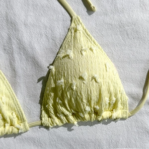 Dettaglio del top bikini a triangolo giallo pallido con texture a pieghe e piccoli pompon