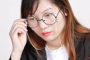 Detail of cream pearl eyewear chain with non-slip rubber loops on black glasses