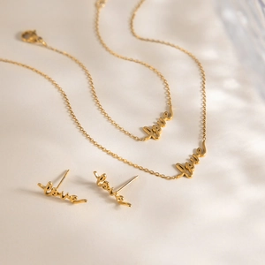 Detail of elegant gold Love letter necklace and earrings set on soft fabric