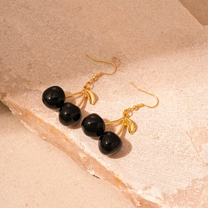 Detail of dark cherry earrings with black resin beads on gold branch on stone