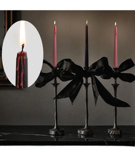 Detailed view of bleeding taper candles on black vintage holders with satin bows