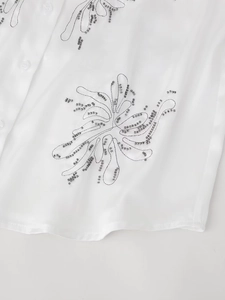 Close-up of white chiffon blouse featuring grey sequin floral embroidery and clear buttons