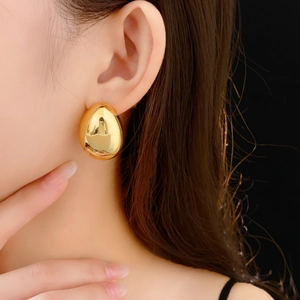Gros plan d'une boucle d'oreille goutte minimaliste plaquée or portée par un mannequin