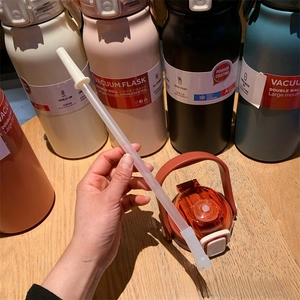 Detail of multi-color stainless steel vacuum flasks with straws on wooden surface