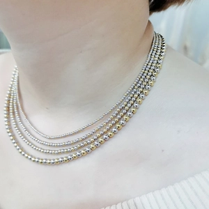 Detail of layered gold and silver bead necklace shown on a model neck with a minimalist style