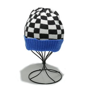 Detail of checkered knit beanie with blue ribbed cuff shown on a metal display stand