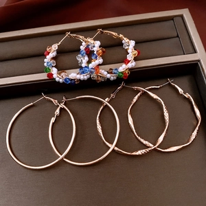Three pairs of gold hoop earrings with colorful beads and textured twists in a jewelry tray