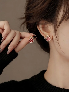 Macro detail of gold plated fortune bag earrings with red enamel and white zircon stones