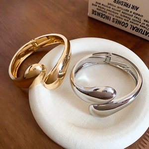 Dettaglio di bracciali metallici profilati e regolabili in finiture oro e argento su ceramica