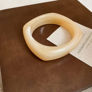 Detailansicht eines cremegelben Acryl-Armreifs in quadratischer Form auf Buch