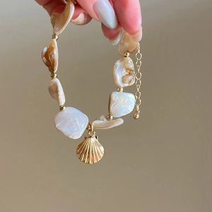 Detailed shot of cream beaded necklace with a golden seashell charm and adjustable chain