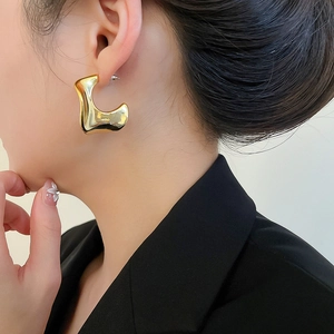 Close-up of model wearing gold chunky twisted C-shaped earrings with a polished finish