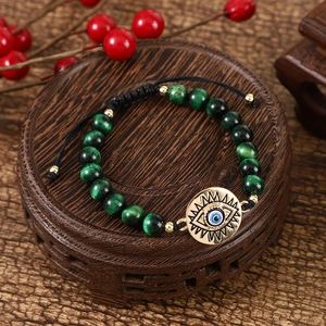 Handmade green tiger eye evil eye bracelet with adjustable black braided cord on wood base