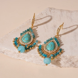 Macro view of vintage gold earrings with turquoise stones and blue beaded tassels on white stone