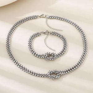 Macro view of silver double-layered knotted necklace and bracelet set on beige fabric