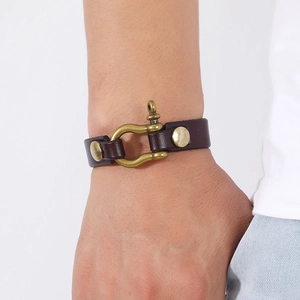 Close-up of a men's dark brown leather bracelet with brass horseshoe buckle and studs