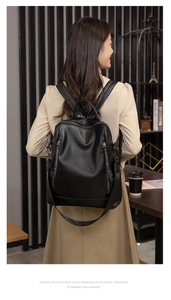 Rear view of a model wearing a black litchi pattern PU leather backpack in a cozy cafe