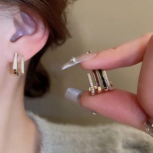 Detail of gold double-layered earrings with white zircon and enamel on a model