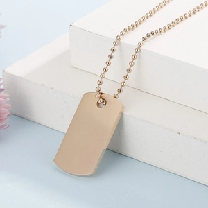 Close-up of golden rectangular dog tag pendant on bead chain against light blue backdrop